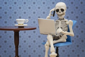 Skeleton talking with smartphone while working with laptop